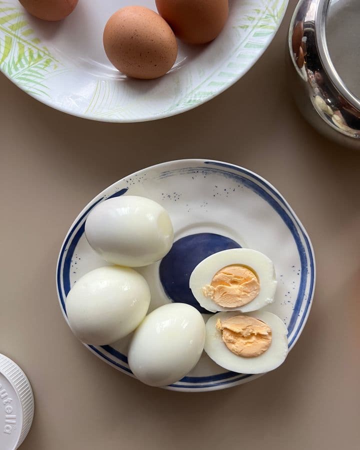Đĩa trứng luộc đã bóc vỏ, một quả cắt đôi lộ lòng đỏ, phía trên là đĩa trứng sống